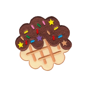 Peut inclure: Un cornet de gaufre au chocolat brun avec des pépites colorées et des étoiles jaunes. Le cornet de gaufre est brodé sur un fond blanc.