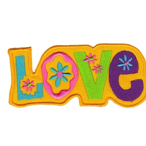 Könnte beinhalten: Ein gelber Filz-Patch mit dem Wort "LOVE" in bunten Buchstaben und Blumen gestickt.