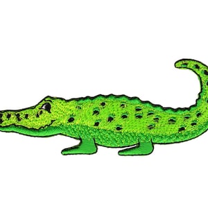 Op de afbeelding: Groene geborduurde alligator-patch met een glimlachend gezicht en een textuur.