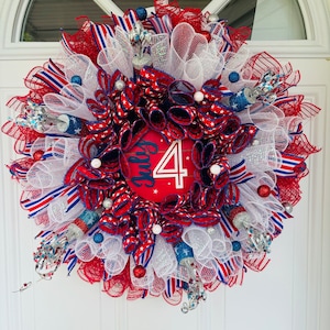 May include: A red, white, and blue Fourth of July wreath with a red sign that says "July 4" and is decorated with white mesh, red and blue ribbon, and silver and blue glitter stars.