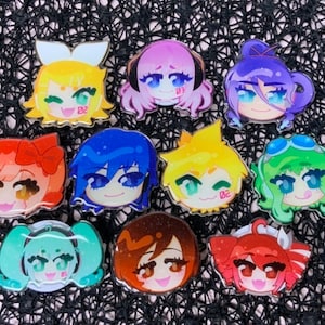 May include: Nine colourful character pins with different expressions. The pins are round and feature anime-style characters with large eyes and bright colours. The characters are wearing various accessories, such as bows, hats and sunglasses.