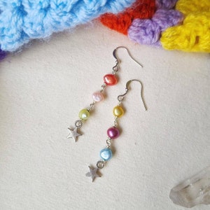 May include: Rainbow coloured pearl earrings with silver star charms. The earrings are on a white background.