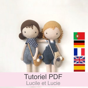 Puede incluir: Dos muñecas de crochet con pelo marrón y rubio, que llevan monos azules y una bufanda azul y blanca. Las muñecas sostienen bolsas de crochet y están de pie sobre un fondo blanco. El texto "Tutoriel PDF Lucile et Lucie" se muestra debajo de las muñecas.