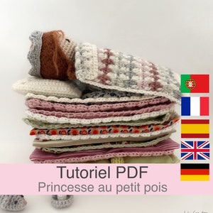 Może przedstawiać: Dziewczynka lalka zrobiona na szydełku z koroną, leżąca na stosie kolorowych poduszek. Tekst "Tutorial PDF Princesse au petit pois" znajduje się na różowym tle.