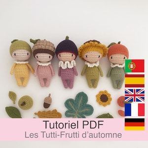 Op de afbeelding: Vijf gehaakte amigurumi poppen in de vorm van fruit en groenten. De poppen dragen verschillende gekleurde outfits en hebben verschillende gezichtsuitdrukkingen. De poppen zijn in een rij op een witte achtergrond gerangschikt. De poppen zijn omringd door gehaakte bladeren, eikels en een zonnebloem.
