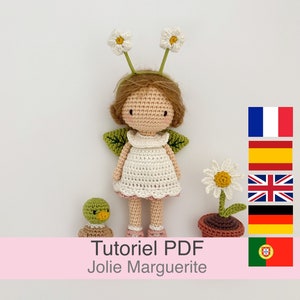 Może przedstawiać: Wzór na szydełku PDF dla uroczej lalki amigurumi z akcentami w postaci kwiatów stokrotek. Lalka ma na sobie białą sukienkę i brązowe włosy. Wzór jest dostępny w języku francuskim, hiszpańskim, angielskim, niemieckim i portugalskim.