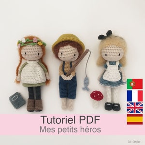 Może przedstawiać: Trzy szydełkowe lalki, dziewczynka z wiankiem kwiatów, chłopiec z wędką i dziewczynka w niebieskiej sukience i kokardką. Lalki stoją na białym tle z tekstem "Tutoriel PDF Mes petits héros" i flagami Portugalii, Francji, Wielkiej Brytanii i Hiszpanii.