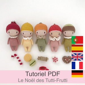 May include: Five crocheted dolls in different colors, each wearing a hat and a bib. The dolls are arranged in a row on a white background. The dolls are surrounded by small crocheted items, including a candy cane, a macaron, a candy, and a heart-shaped cookie. The text "Tutoriel PDF Le No&euml;l des Tutti-Frutti" is written in pink at the bottom of the image. The image also includes flags for Portugal, Spain, the United Kingdom, France, and Germany.