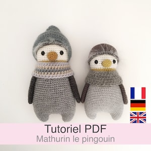 May include: Two crocheted penguin amigurumi toys, one larger than the other, both wearing grey scarves and hats. The larger penguin has a grey hat and the smaller penguin has a brown hat. The penguins are both standing on a white surface. The text "Tutoriel PDF Mathurin le pingouin" is at the bottom of the image.