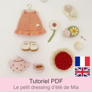 Puede incluir: Un conjunto de ganchillo que incluye un vestido color melocotón en una percha, zapatos blancos con suela marrón, una tetera y taza con puntos rojos, una tarta de frutos rojos, una tortuga verde con caparazón de flor y dulces en una bandeja.