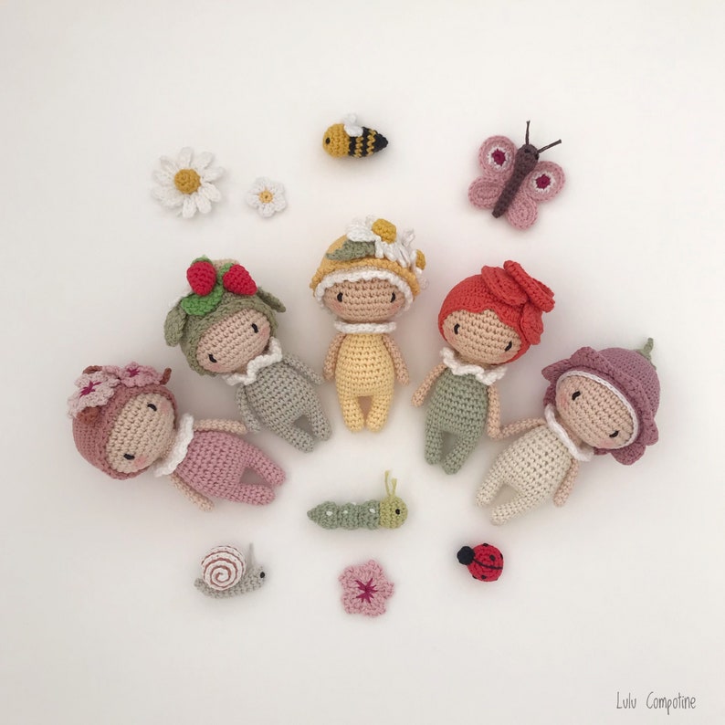 Puede incluir: Una colecci&oacute;n de mu&ntilde;ecas y peque&ntilde;as criaturas hechas a mano con ganchillo, incluyendo una abeja, una mariposa, una oruga, un caracol, una mariquita y flores. Las mu&ntilde;ecas est&aacute;n vestidas con varios colores y adornadas con sombreros y accesorios florales.