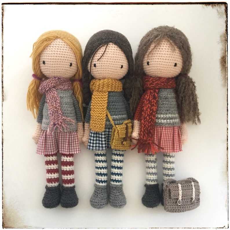 Peut inclure: Trois poup&eacute;es en crochet portant des &eacute;charpes et des jupes color&eacute;es. Chaque poup&eacute;e porte une &eacute;charpe et une jupe de couleur diff&eacute;rente. Les poup&eacute;es sont debout sur une surface blanche.