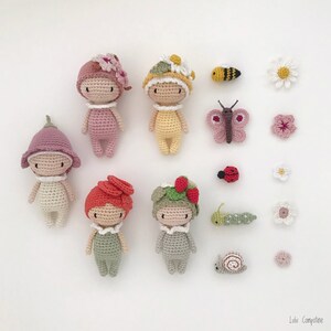 Puede incluir: Una colecci&oacute;n de mu&ntilde;ecas de ganchillo hechas a mano y peque&ntilde;os objetos decorativos. Las mu&ntilde;ecas son de varios colores, con sombreros con temas de flores y frutas. Los elementos adicionales incluyen una mariposa, una abeja, una mariquita, una oruga, un caracol y flores.