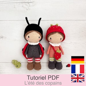 Może przedstawiać: Dwie ręcznie robione szydełkowe lalki, jedna przebrana za biedronkę, a druga za truskawkę. Lalka biedronka ma czarny kapelusz z czułkami i czerwonymi skrzydłami. Lalka truskawka nosi czerwony kapelusz i nosi torebkę z truskawką. Tekst "Tutoriel PDF L'été des copains" znajduje się na dole.