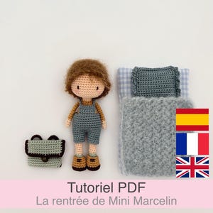 Może przedstawiać: Szydełkowa lalka z brązowymi włosami i niebieskimi ogrodniczkami, pasującym plecakiem i miniaturowym łóżkiem z szarym kocem i poduszką. Obraz zawiera również tekst "Tutoriel PDF La rentrée de Mini Marcelin."