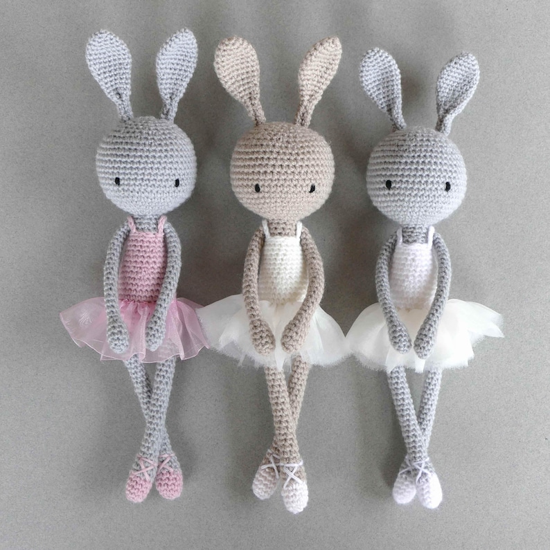Puede incluir: Tres mu&ntilde;ecas de conejo de crochet vestidas con tut&uacute;s de bailarina. Los conejos son grises, beige y grises con tut&uacute;s rosas, blancos y blancos.