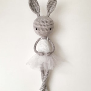 Puede incluir: Un conejito de crochet gris que lleva un tut&uacute; blanco con una falda de tul. El conejito tiene orejas largas y est&aacute; de pie sobre un fondo blanco.