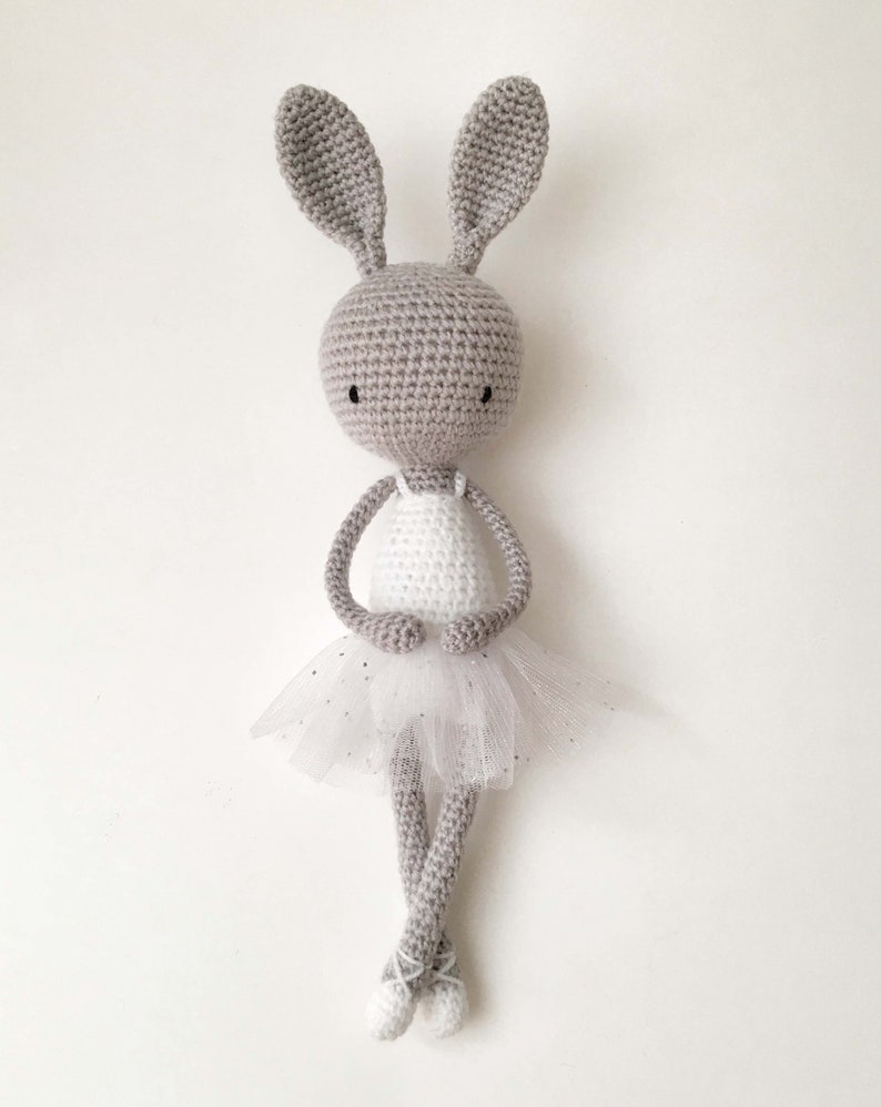 Puede incluir: Un conejito de crochet gris que lleva un tut&uacute; blanco con una falda de tul. El conejito tiene orejas largas y est&aacute; de pie sobre un fondo blanco.