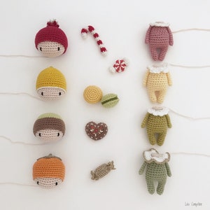 May include: A collection of handmade crocheted amigurumi dolls, each with a different color and design. The dolls are arranged in a row on a white background, with various small crocheted items scattered around them.