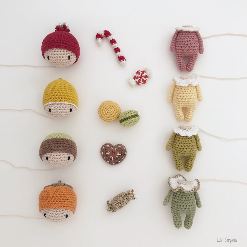 May include: A collection of handmade crocheted amigurumi dolls, each with a different color and design. The dolls are arranged in a row on a white background, with various small crocheted items scattered around them.