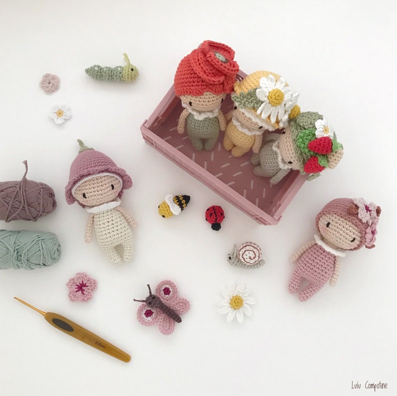 Puede incluir: Una colecci&oacute;n de mu&ntilde;ecas de ganchillo hechas a mano y criaturas en miniatura, incluyendo una oruga, una abeja, una mariquita y un caracol. Las mu&ntilde;ecas visten sombreros y trajes con tem&aacute;tica floral, con hilo y un ganchillo.