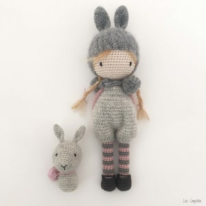 Pode incluir: Uma boneca e uma cabe&ccedil;a de coelho feitas &agrave; m&atilde;o em croch&ecirc;. A boneca usa um chap&eacute;u de coelho cinza, macac&atilde;o e meias listradas. A cabe&ccedil;a do coelho tem um len&ccedil;o rosa. A boneca tem cerca de 25 cm de altura.