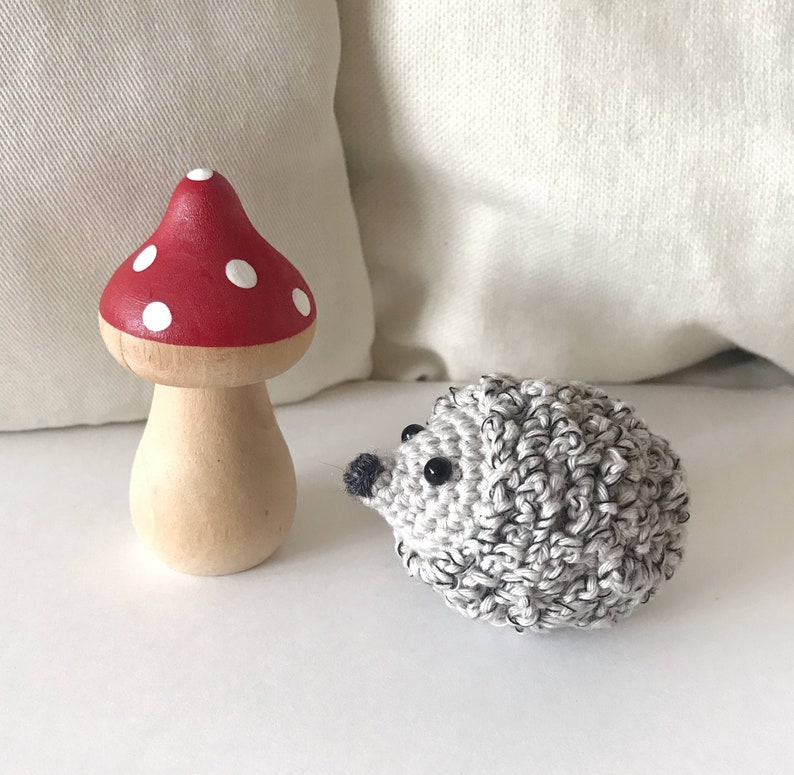 K&ouml;nnte beinhalten: Ein geh&auml;keltes Igelspielzeug mit schwarzen Augen und ein rotes und wei&szlig;es Holzpilzspielzeug.