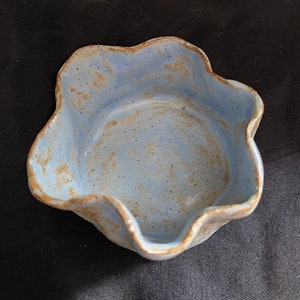 May include: A light blue ceramic bowl with a wavy rim and a speckled glaze. The bowl has a rustic, handmade look.