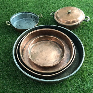 Puede incluir: Conjunto de cuatro ollas y sartenes de cobre, que incluyen una olla con tapa, una sartén grande, una sartén mediana y una sartén pequeña. Las ollas y sartenes están hechas de cobre y tienen un acabado brillante.