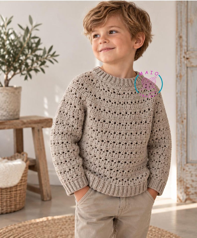 Pu&ograve; includere: Un maglione a maniche lunghe all'uncinetto color beige con scollo rotondo, polsini a coste e orlo a coste. Il maglione presenta un motivo a punto traforato ripetuto su tutto il corpo e le maniche. &Egrave; visibile un logo circolare con il testo MAIO.