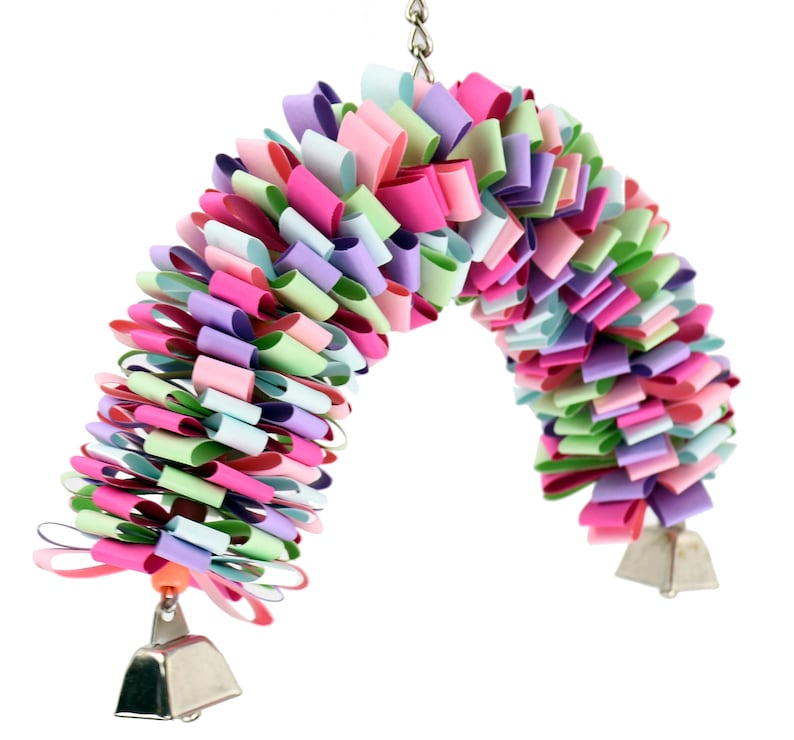 May include: A colorful, multi-layered, paper bird toy with bells hanging from the bottom. The toy is made of pink, purple, green, and blue paper.
