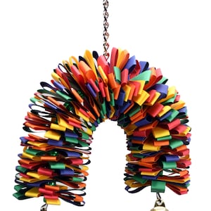 May include: A colorful, multi-layered, ribbon toy for birds. The toy is shaped like an arch and has two bells hanging from the bottom. The toy is attached to a metal chain.