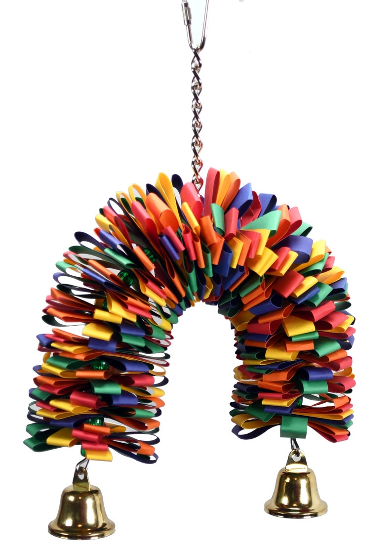 May include: A colorful, multi-layered, ribbon toy for birds. The toy is shaped like an arch and has two bells hanging from the bottom. The toy is attached to a metal chain.