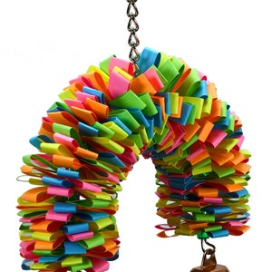 May include: A colorful rainbow-colored bird toy with two bells hanging from the bottom. The toy is made of paper strips and is attached to a silver chain.