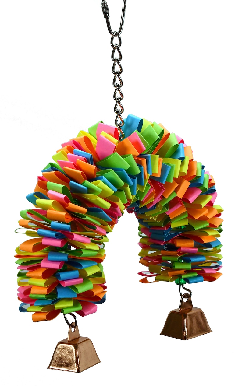 May include: A colorful rainbow-colored bird toy with two bells hanging from the bottom. The toy is made of paper strips and is attached to a silver chain.