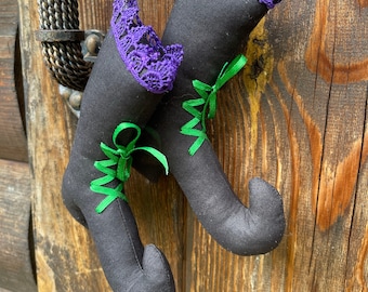 Puede incluir: Dos calcetines de bota de bruja negros con detalles de cinta verde y morada colgando de una puerta de madera.