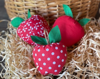 May include: A wicker basket filled with red fabric apples with white polka dots and white floral patterns. The apples are sitting on a bed of shredded paper.