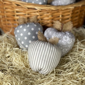Può includere: Un cesto pieno di mele di stoffa grigie e bianche con motivi a pois, floreali e a righe. Le mele sono su un letto di carta triturata.