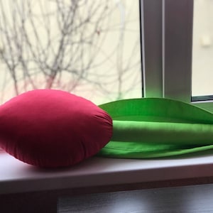 May include: A red and green fabric tulip pillow. The pillow is shaped like a tulip with a red flower and a green stem and leaf.