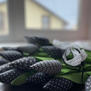 May include: A bouquet of black and white fabric tulips with green stems and leaves. The tulips have different patterns, including polka dots, zigzags, and floral prints.