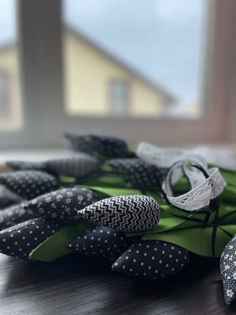 May include: A bouquet of black and white fabric tulips with green stems and leaves. The tulips have different patterns, including polka dots, zigzags, and floral prints.
