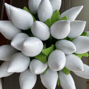 May include: A close-up of a bouquet of white fabric tulips with green fabric leaves. The tulips are tightly clustered, creating a full, textured appearance. The fabric has a slightly textured appearance, and the overall effect is soft and delicate.