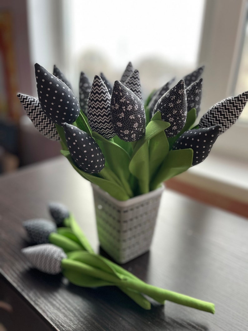 May include: A bouquet of black and white fabric tulips in a black and white striped vase. The tulips have different patterns, including polka dots, zigzags, and floral prints.
