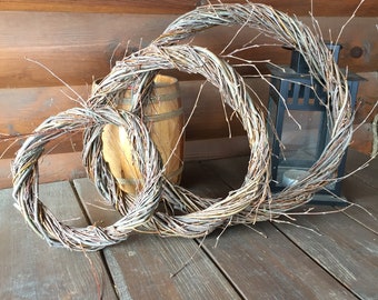 May include: Three woven wreaths made of natural twigs, arranged in a circle on a wooden surface. The wreaths are different sizes and are stacked on top of each other.