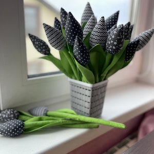 May include: A bouquet of black and white fabric tulips in a gray planter. The tulips have different patterns, including polka dots, zigzags, and floral prints.