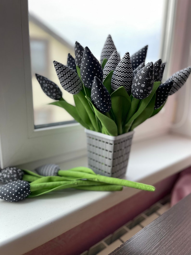 May include: A bouquet of black and white fabric tulips in a gray planter. The tulips have different patterns, including polka dots, zigzags, and floral prints.