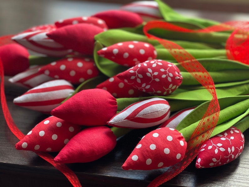 Puede incluir: Un ramo de tulipanes de tela hechos a mano en rojo, blanco y verde. Los tulipanes tienen diferentes patrones, incluyendo lunares, rayas y hojas. Los tallos son verdes y el ramo est&aacute; atado con una cinta roja.