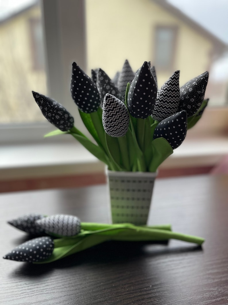 May include: A bouquet of black and white fabric tulips in a white and black polka dot vase. The tulips have different patterns, including polka dots, zigzags, and floral prints.