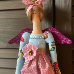 May include: A handmade doll with a blue dress, pink skirt, and wings. The doll has brown hair and a pink headband. The doll is wearing a flower on her dress.