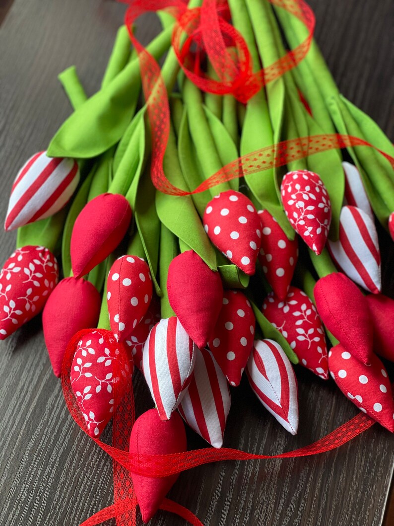Puede incluir: Un ramo de tulipanes de tela roja con lunares blancos, rayas y patrones florales. Los tulipanes est&aacute;n atados con una cinta roja y tallos verdes.